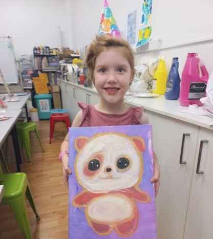 girl in party hat holding her finished cute panda painting